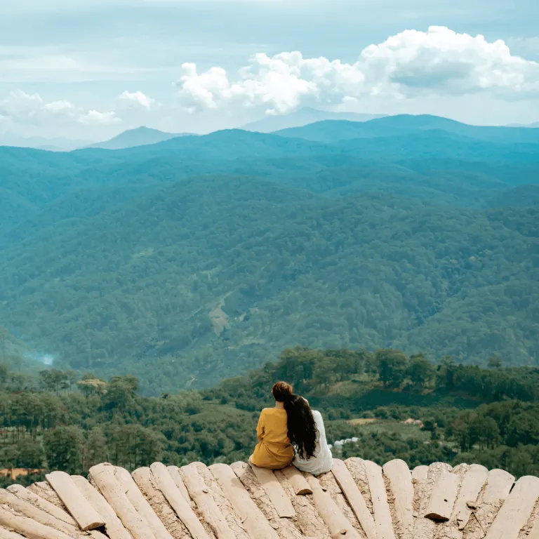 two girls sitting on wood overlooking a mountainous scenery