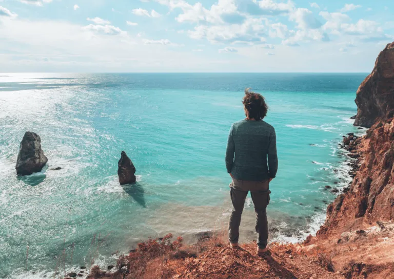 single man standing on the edge of a cliff overlooking a beach