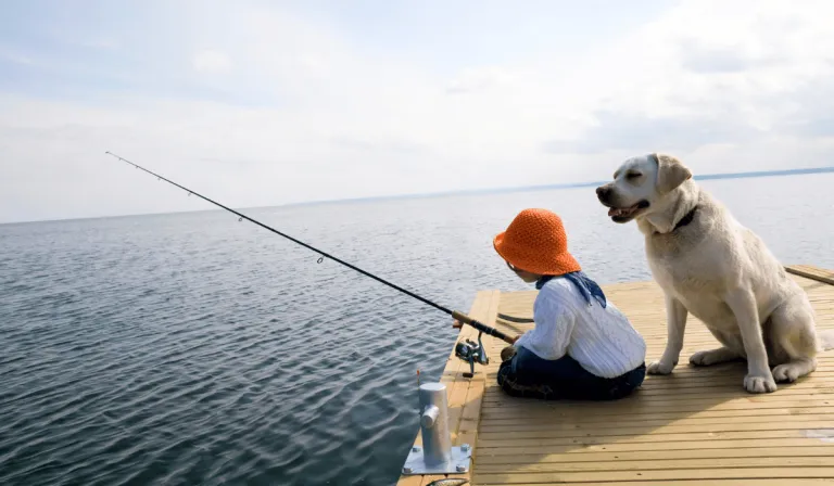 girl fishing with dog beside her